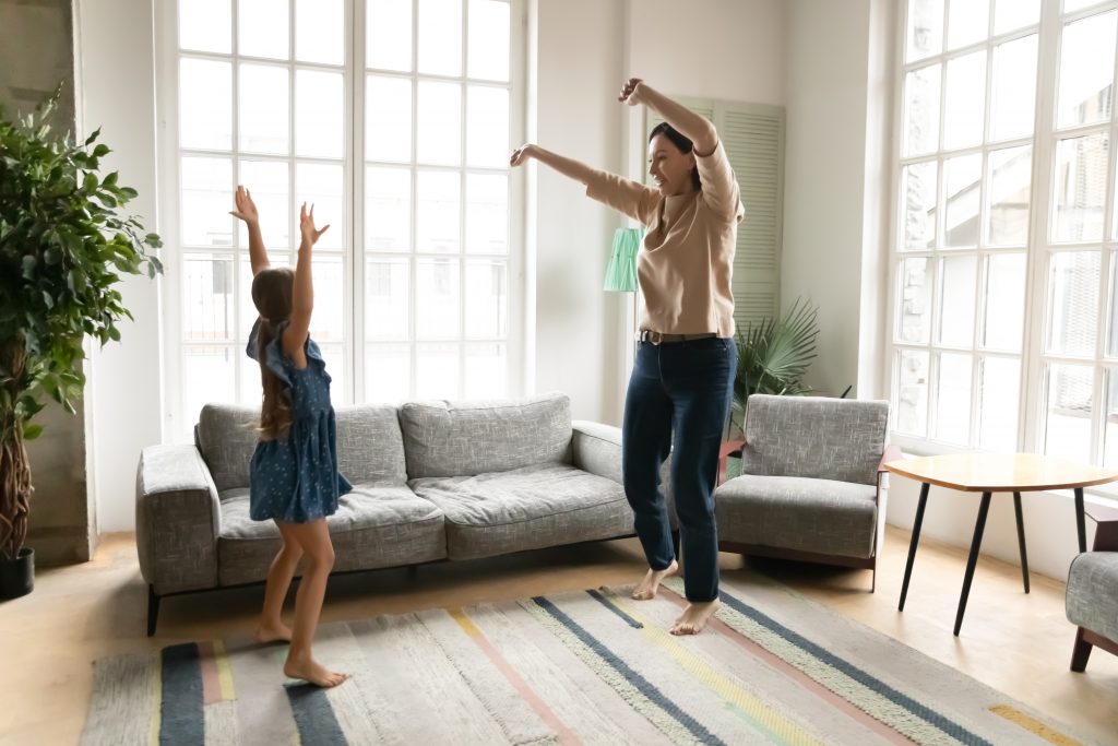 Energetic grandmother dancing in living room with granddaughter