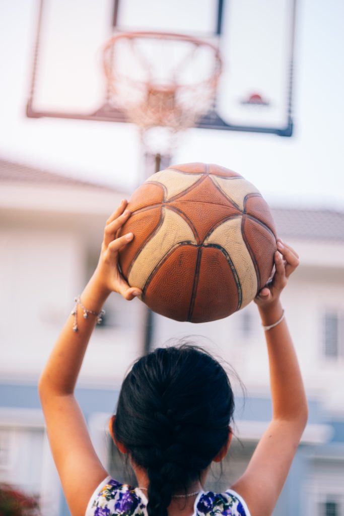Little girl shooting basket and playing basketball at home